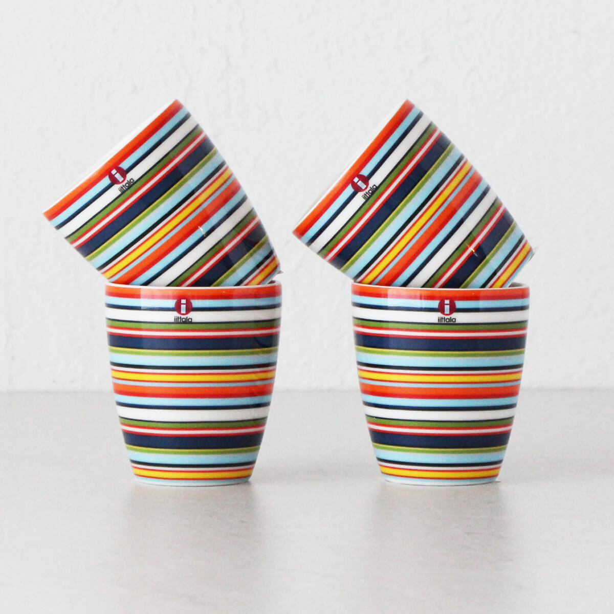Four ceramic cups stacked in pairs, decorated with bright horizontal stripes in red, blue, yellow, and green.