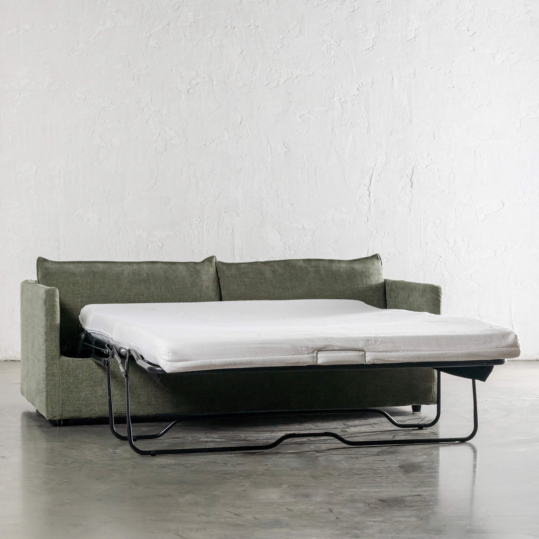 Green sofa bed with white mattress against a white wall.