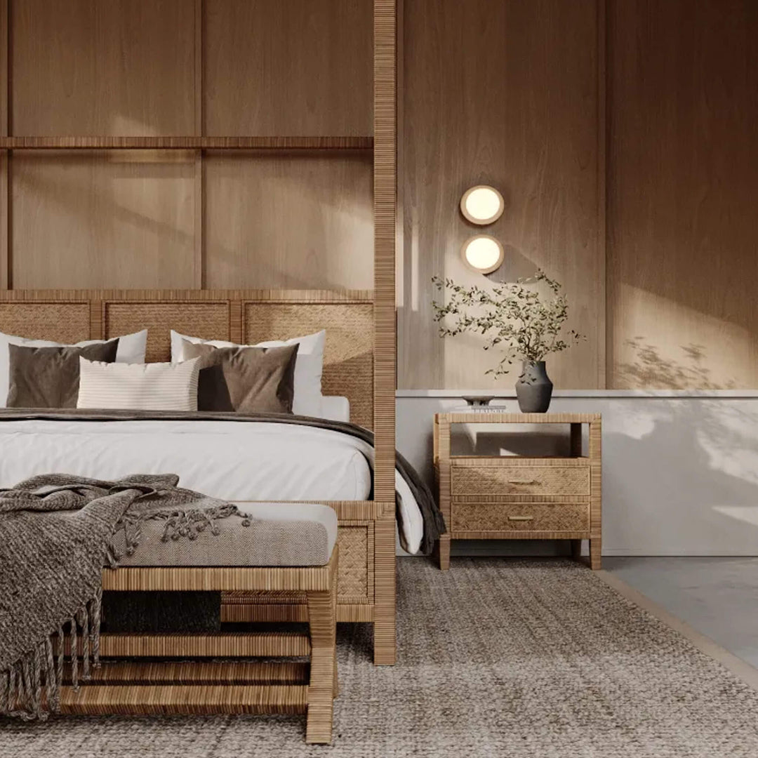 A contemporary bedroom featuring a woven rattan four-poster canopy bed, a matching bedside table, and an upholstered bench against wood-panelled walls.